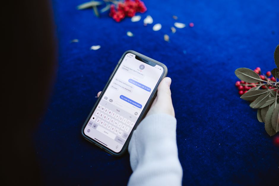 A person holding a smartphone displaying text messages on a blue surface with flowers.