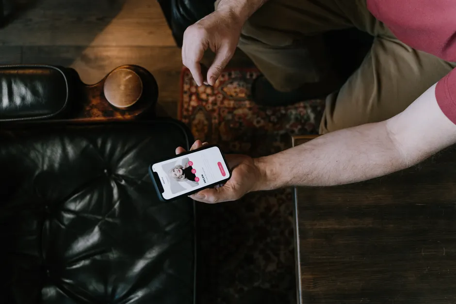 Les applications de rencontre rendent-elles plus seuls? A person holding a smartphone with a dating app displayed while sitting on a leather chair.