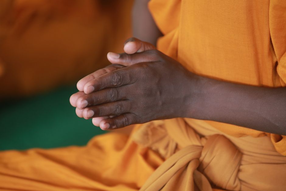 A person in orange robes meditating with hands in prayer position, symbolizing peace and spirituality.