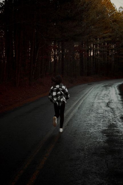 A person running along a wet forest road during a gloomy day, captured from behind.