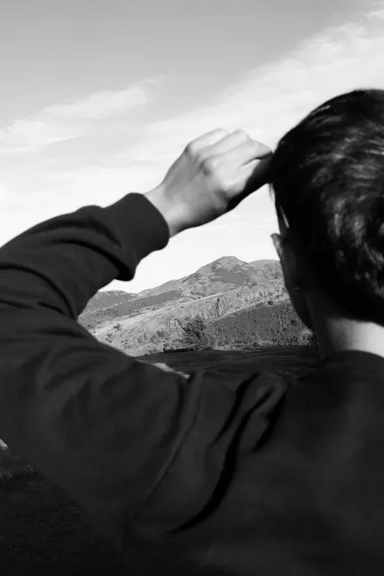 A person seen from behind looking at a mountain landscape in a black and white photograph.