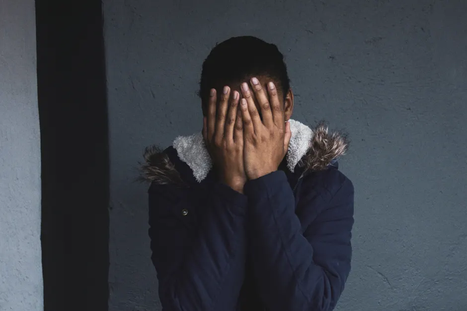A person stands with their face covered by hands, creating a mysterious and thoughtful mood.
