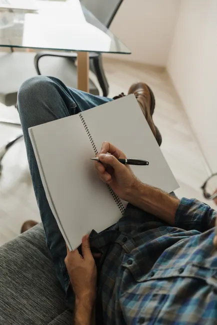 A person writing in a notebook while relaxing on a couch in a modern indoor setting.
