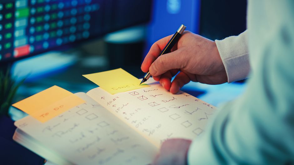 A person writing in a planner with a task checklist on a desk, fostering productivity.