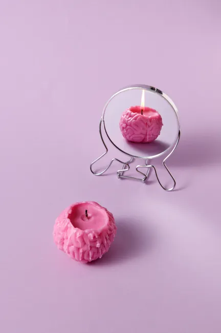 A pink brain-shaped candle reflected in a mirror on a pastel background.