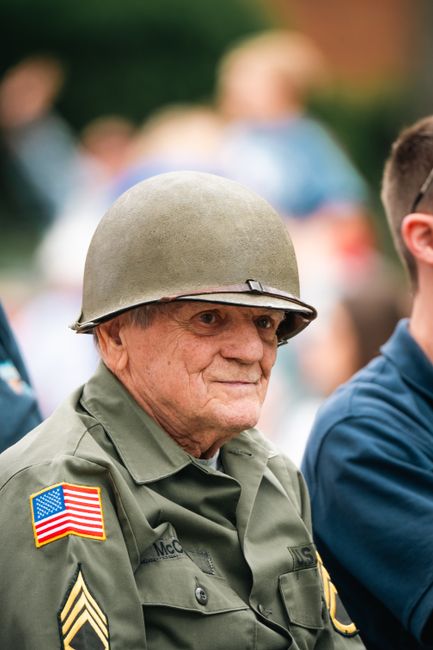 A senior veteran wearing a military uniform and helmet at a public event, symbolizing honor and service.