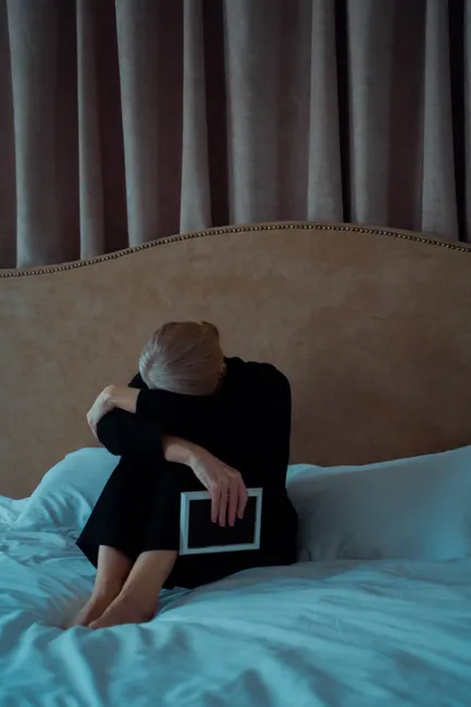 A senior woman sits on a bed holding a photo frame, expressing loneliness and grief.