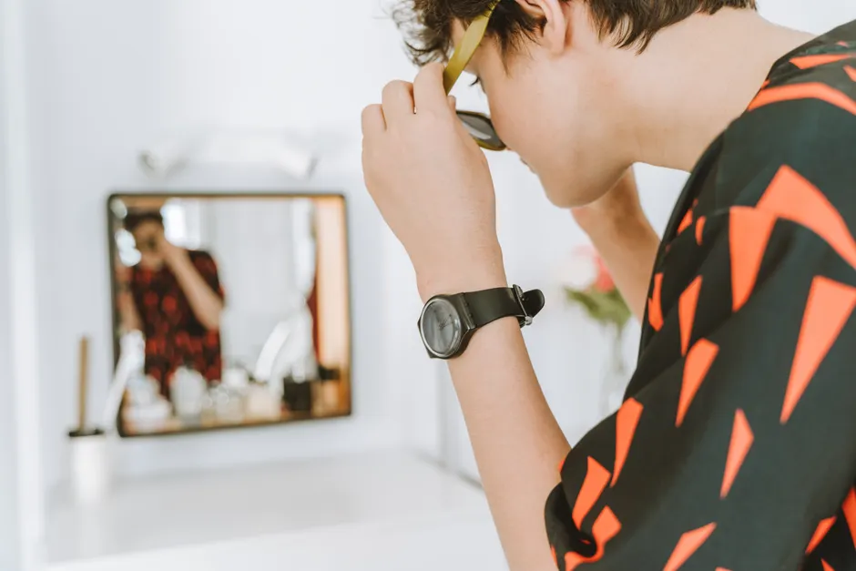 Égocentrisme adolescent : quand tous les regards semblent braqués A stylish teenager adjusts sunglasses while looking in a mirror, embodying modern fashion trends.