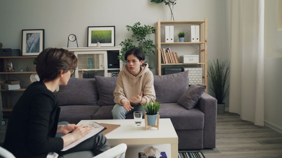 A teenager discusses issues with a therapist in a modern consultation room.