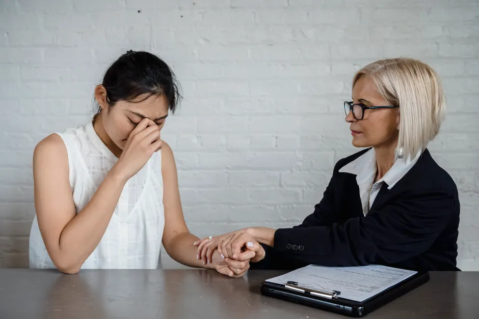 A therapist consoles a young woman dealing with emotional distress in a professional setting.