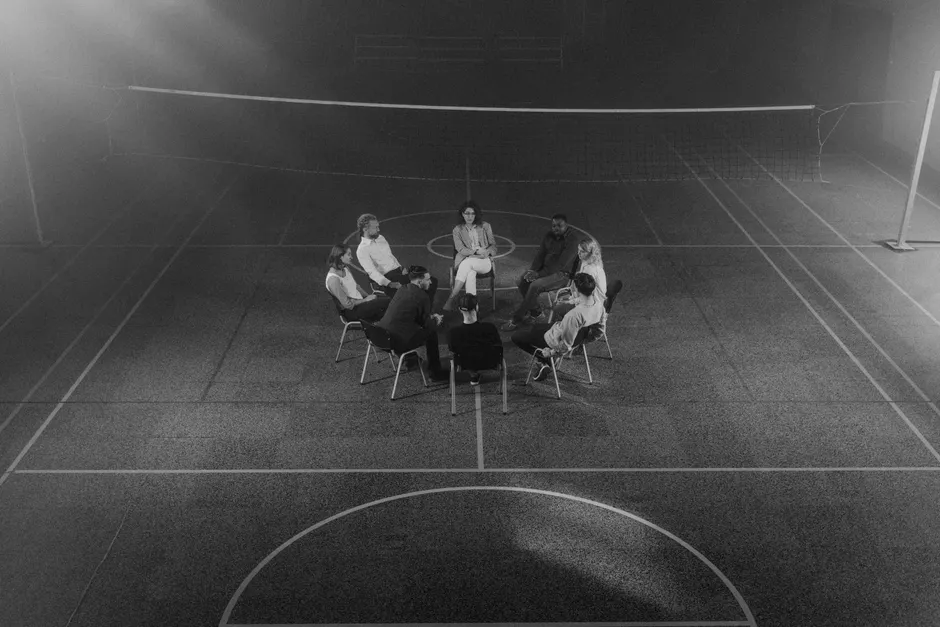 A therapy group sitting in a circle in a dimly lit sports hall.