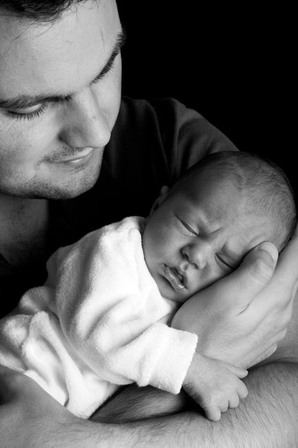 A touching black and white portrait of a father holding his sleeping newborn baby.