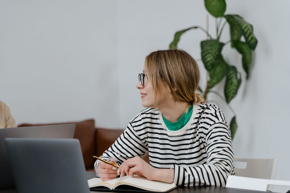 Monotropisme : quand l’attention emprunte un tunnel A woman in glasses sits at a desk, writing in a notebook with a laptop nearby, indoors.