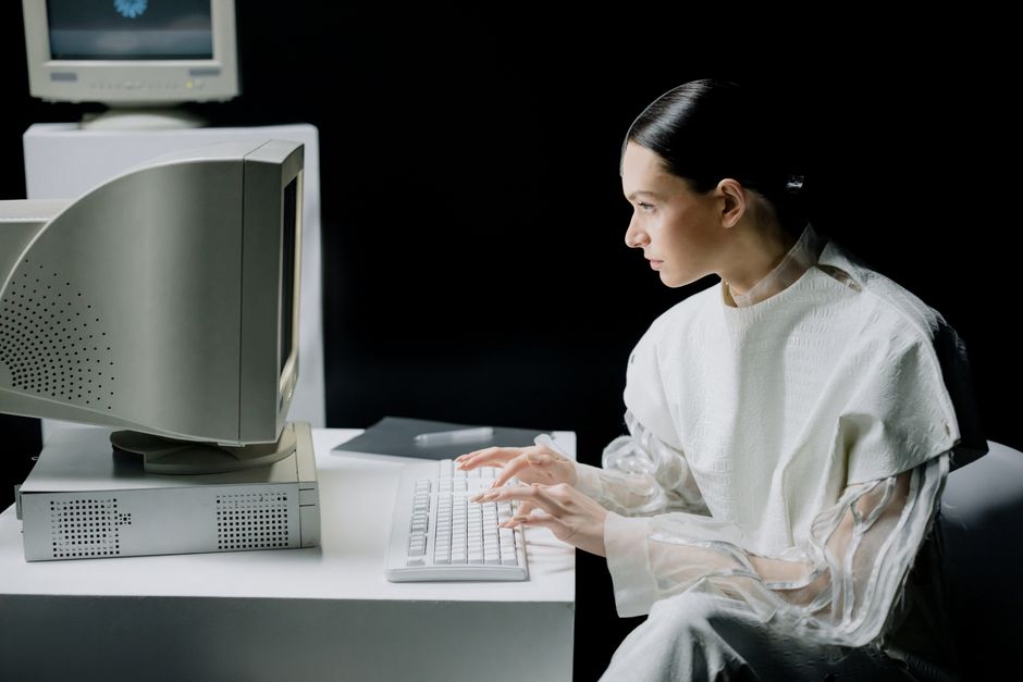 A woman in modern attire using a vintage computer in a dark setting, blending past and future.