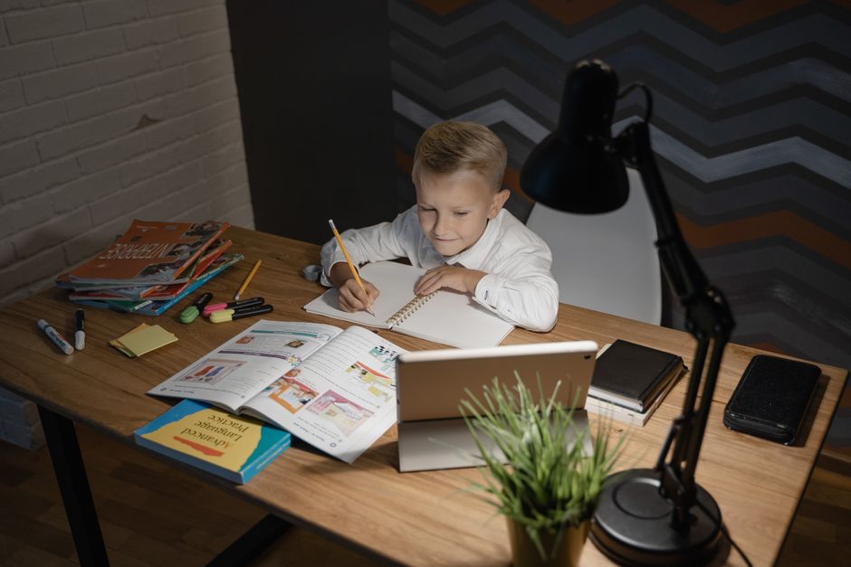 TDAH inattentif chez l’enfant : quand le calme masque la difficulté A young boy focused on studying at a wooden table with a tablet and books nearby under a desk lamp.