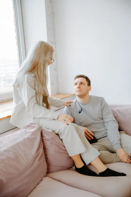 A young couple sitting on a sofa engaged in a meaningful conversation. Bright indoor setting.