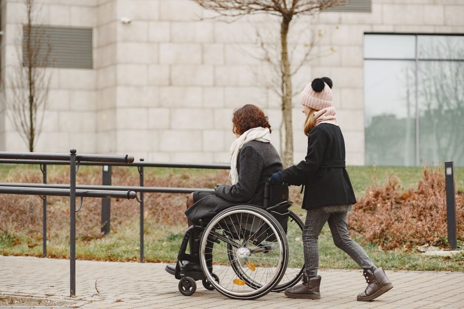 A young girl helps a woman in a wheelchair on a sidewalk, showing care and support.