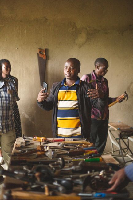 Adults engaged in a community workshop session in Kasese, Uganda surrounded by hand tools. Indoor setting.