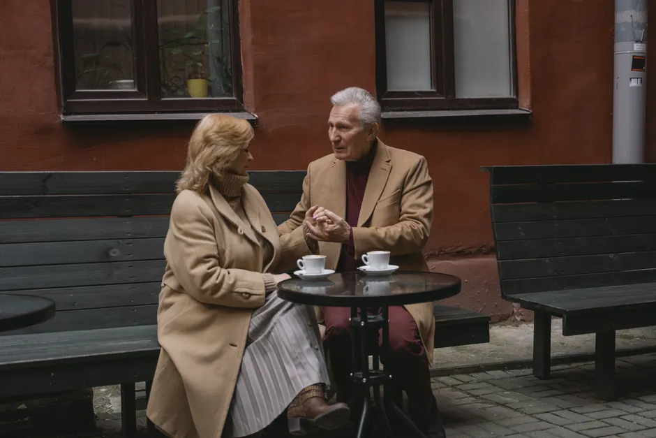 An elderly couple enjoys a conversation over coffee at an outdoor cafe.