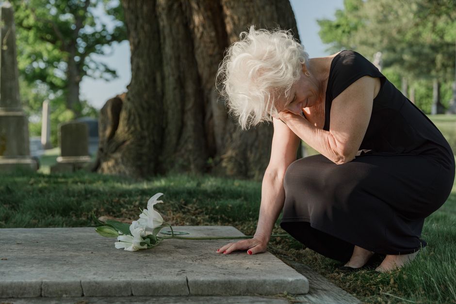 Les cinq étapes du deuil ne sont pas un mode d’emploi An elderly woman grieving at a gravesite, conveying sorrow and loss in a serene cemetery setting.