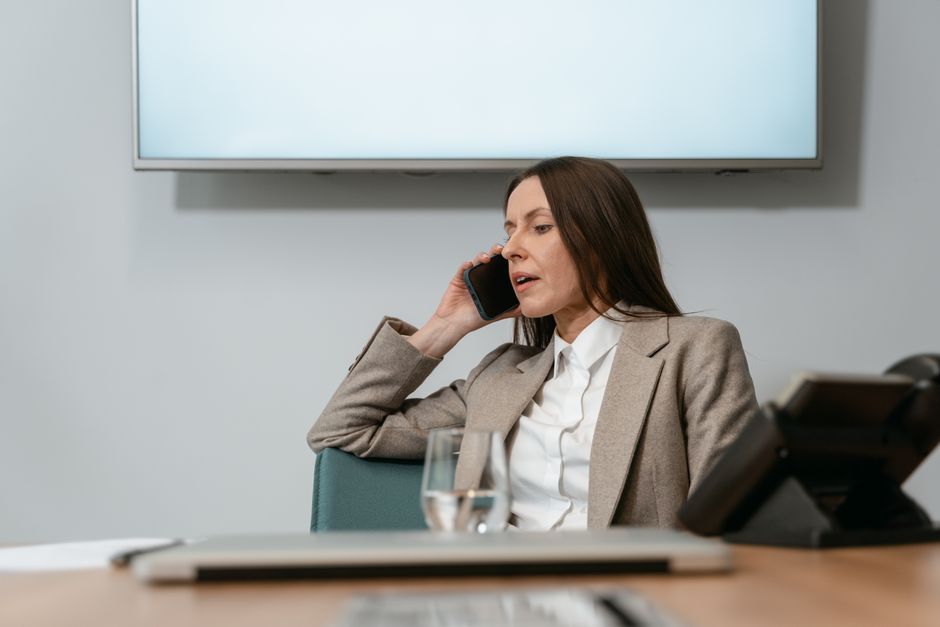 Businesswoman in a blazer making a phone call in an office setting, engaging in a conversation.