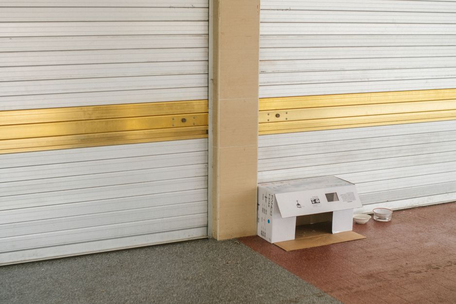 Cardboard shelter setup near garage doors with bowls outside in Singapore.