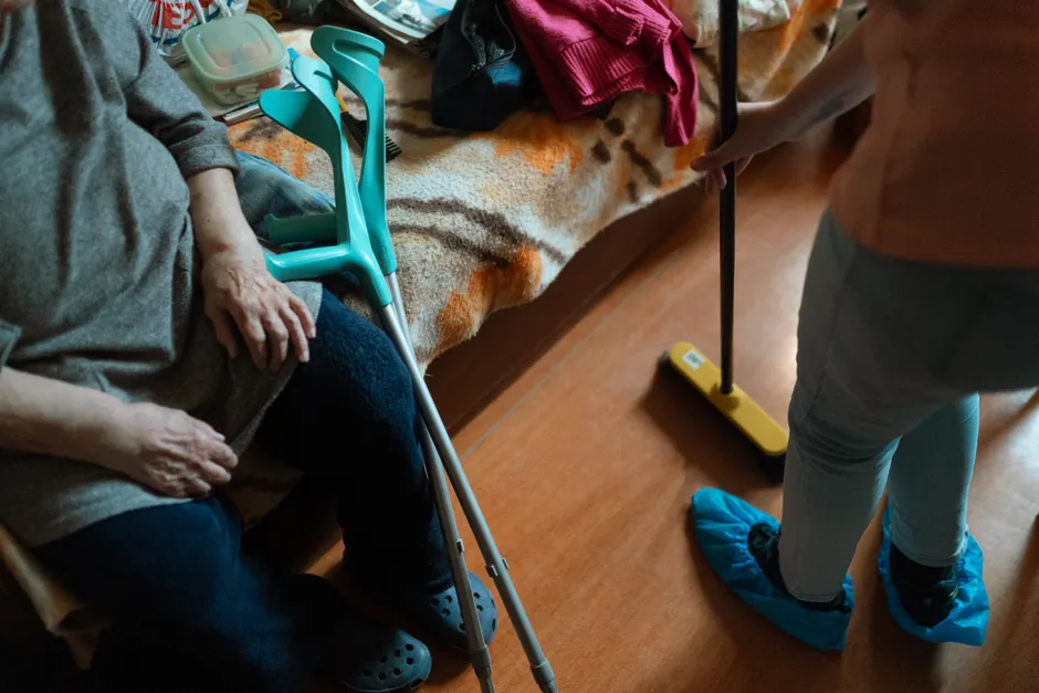 Aidant d’une personne vivant avec une schizophrénie : aider sans s’épuiser Caregiver helps an elderly woman with cleaning tasks, showcasing home care support.