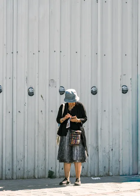 Casual woman stands against a corrugated wall, checking her phone in a city setting.