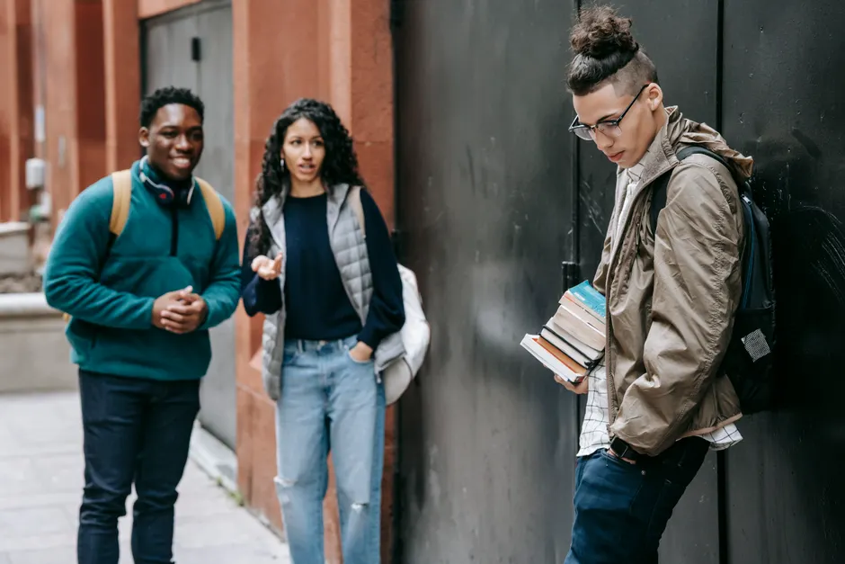 Cheerful multiracial students with backpacks standing near university building and bullying friend with books