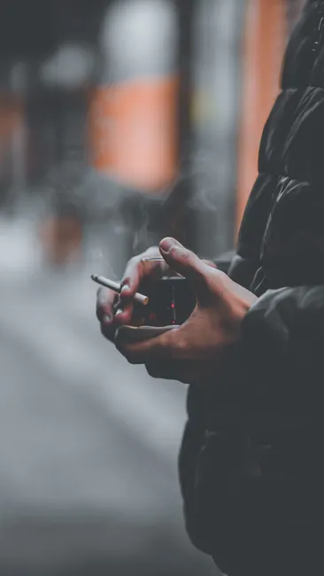 Close-up of a person holding a cigarette with smoke, creating a moody atmosphere.