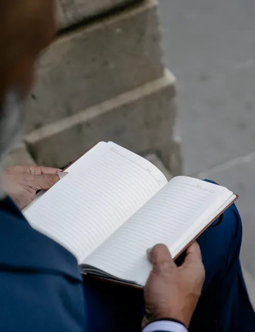 Close-up of a person holding an open notebook while seated outdoors, showing blank pages.