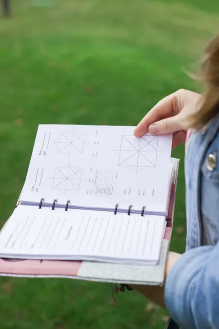 Close-up of a person holding an open planner outdoors on a green lawn, focusing on bullet journaling.