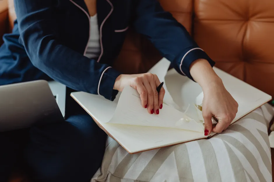 Close-up of a person tearing a page from a notebook while seated on a couch.