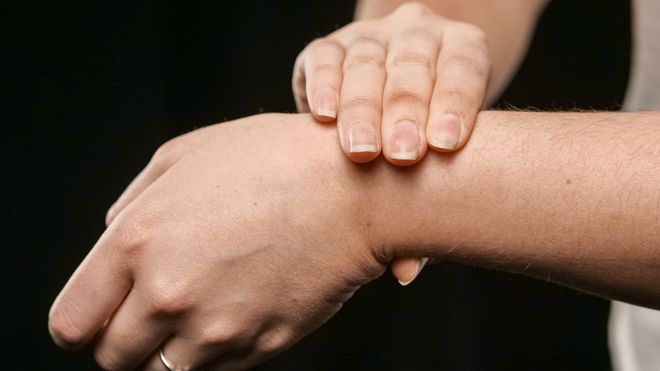 Close-up of a person's hands pressing their wrist, focusing on skin and texture.