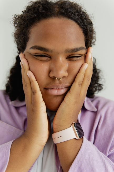 Close-up of a woman with curly hair and septum piercing touching her face, wearing a wristwatch.