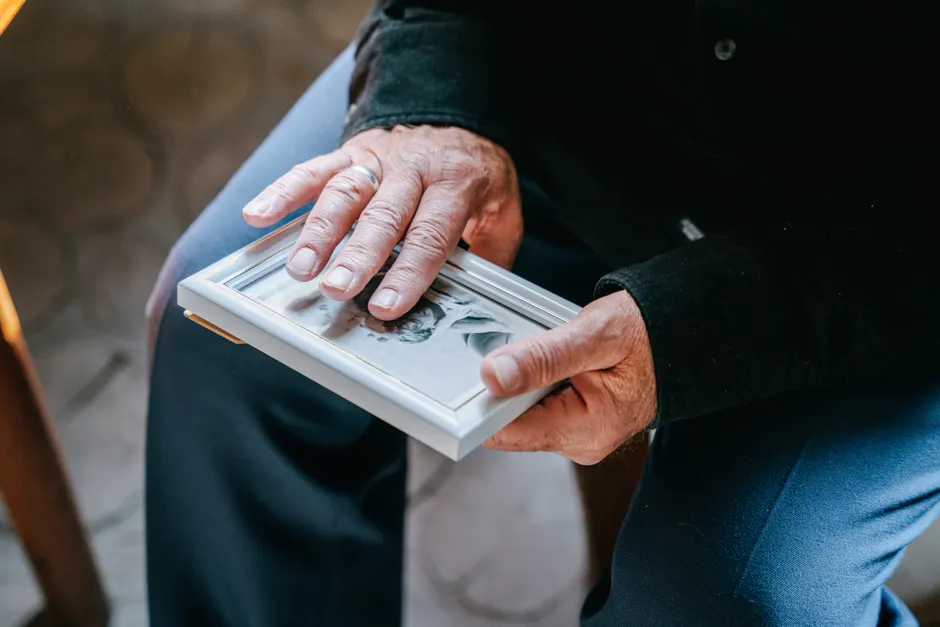 Deuil : avancer sans oublier, ce que la psychologie montre Close-up of elderly hands holding a framed photograph, reflecting nostalgia and emotion.