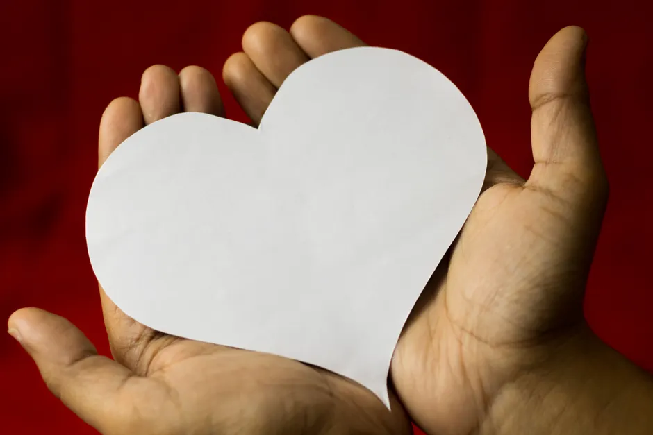 Anxiété et palpitations : ce que le rythme cardiaque peut vraiment dire Close-up of hands cradling a heart-shaped paper, symbolizing love on a red background.