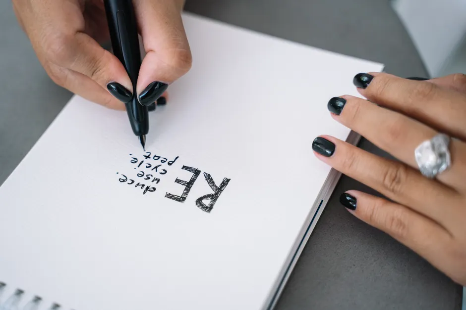 Close-up of hands writing 'Reuse, Recycle, Repeat' on paper, promoting environmental awareness.