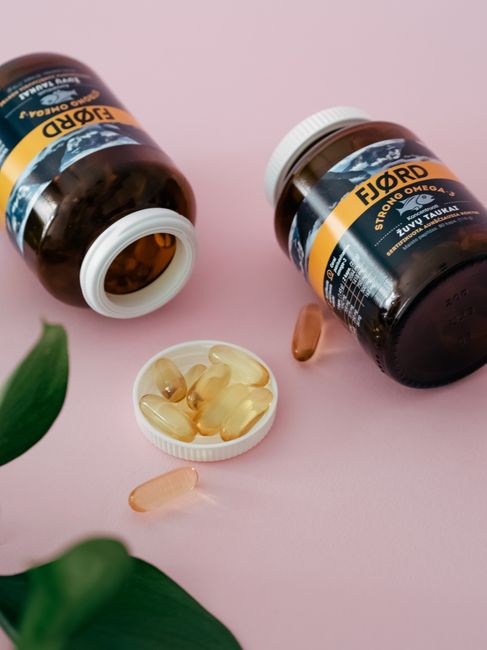 Close-up of omega 3 supplement bottles and capsules on a pink surface.
