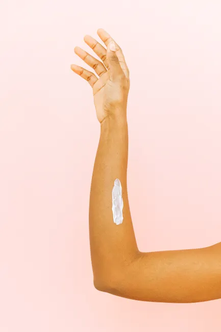 Crop clean hand of young woman with cosmetic treat cream hand lotion placed on inner part of forearm on pink isolated background