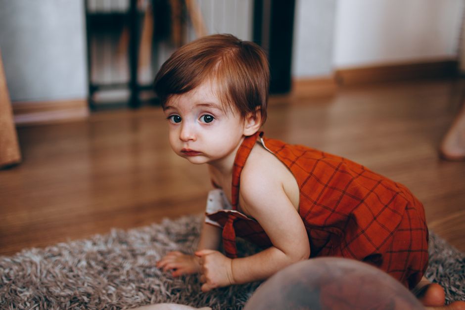 Crises de colère chez l’enfant : quand s’inquiéter et comment réagir Cute toddler in red outfit crawling on a carpeted floor indoors, exploring the room.