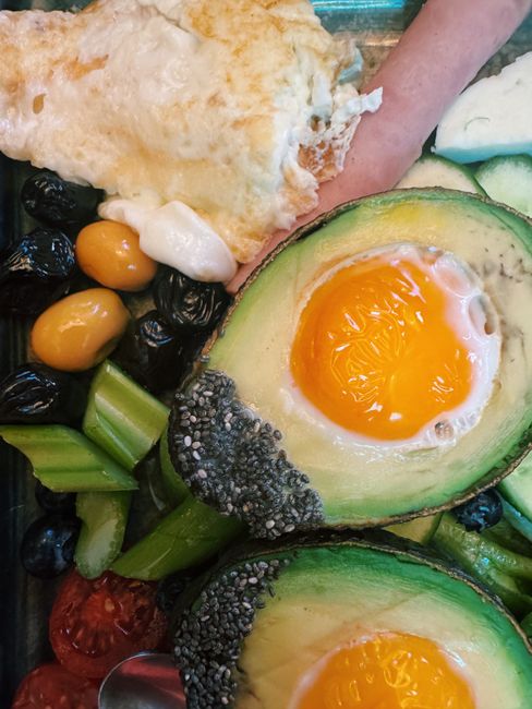 Delicious breakfast featuring avocado, fried eggs, vegetables and fruits.