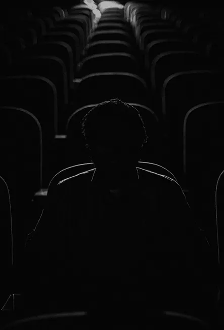 Dramatic silhouette of a person sitting alone in a shadowy cinema hall, creating a moody ambience.