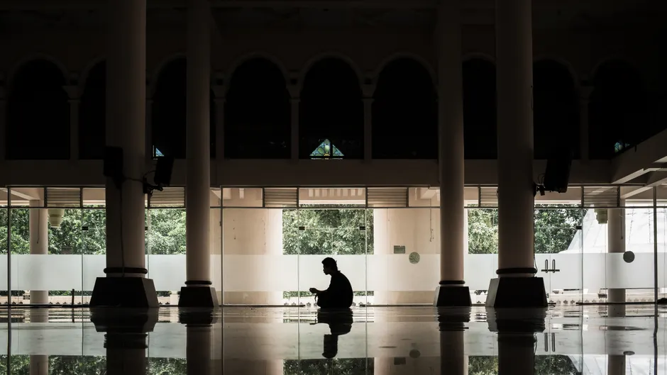 Elegant silhouette of a person indoors, surrounded by tall pillars and reflective flooring, creating a calm and serene atmosphere.