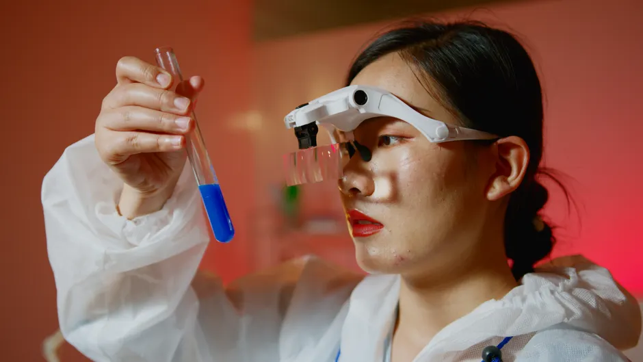 Female scientist examining a test tube with blue liquid in a laboratory setting.