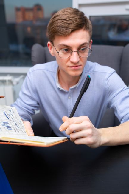Focused man with glasses writing in notebook at a modern desk.
