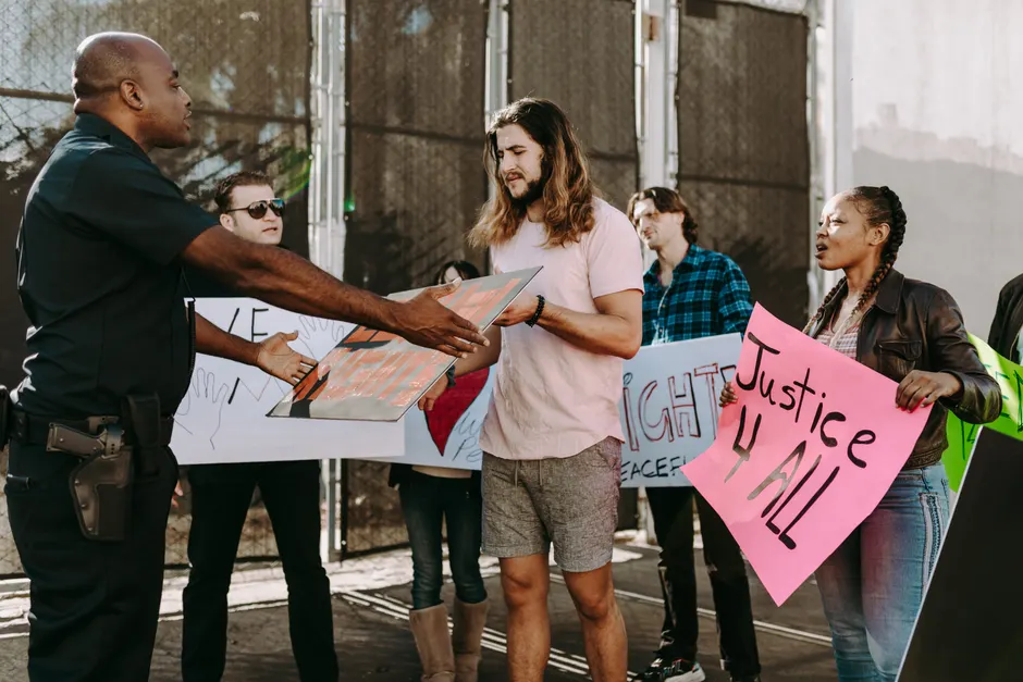 Group of diverse people peacefully protesting with signs and a police officer present.