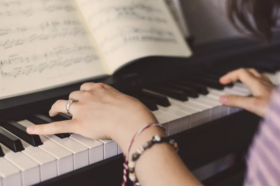 Hands playing piano with sheet music in the background, showcasing musical skill.