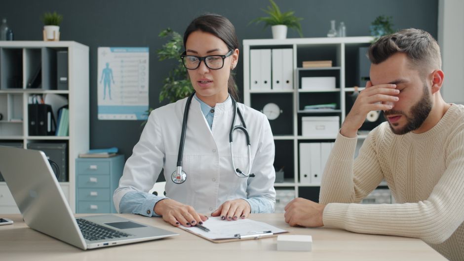 Healthcare professional discussing with patient in doctor's office. Stress and concern are evident.