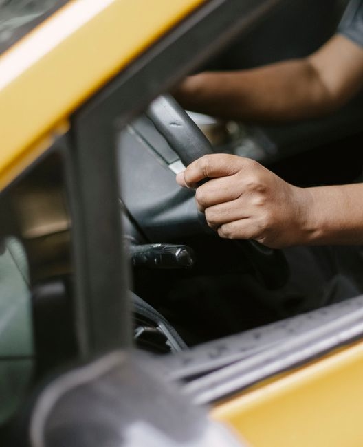 High angle of crop anonymous male driver sitting in taxi with hands on steering wheel while waiting for passenger on city street